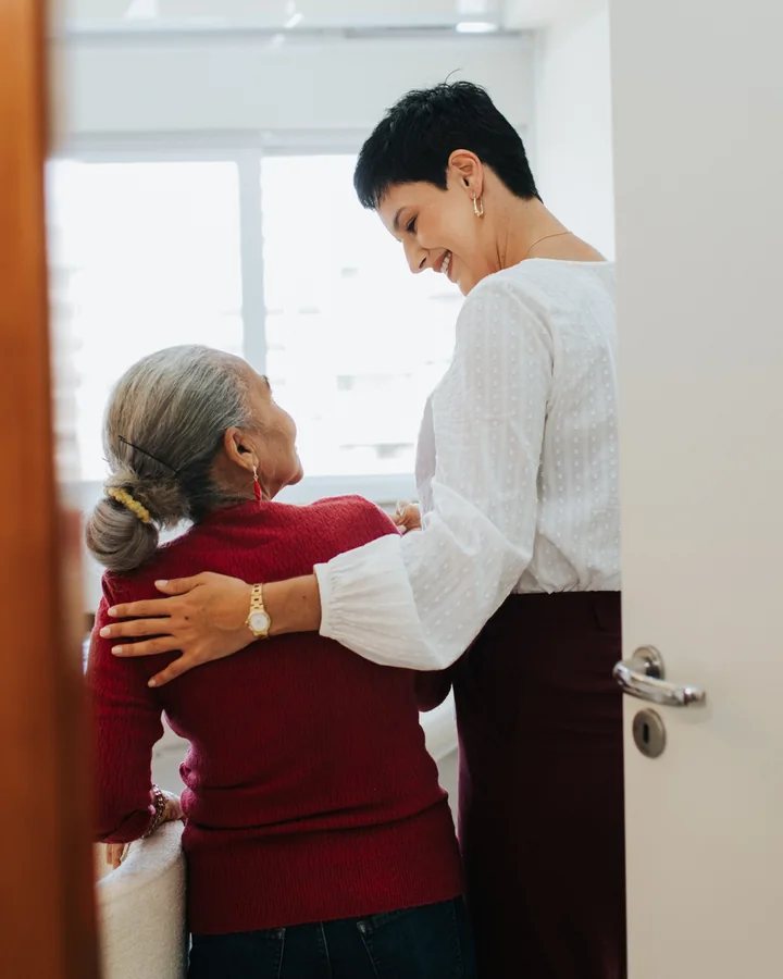 Karine recebe uma paciente idosa à porta do consultório